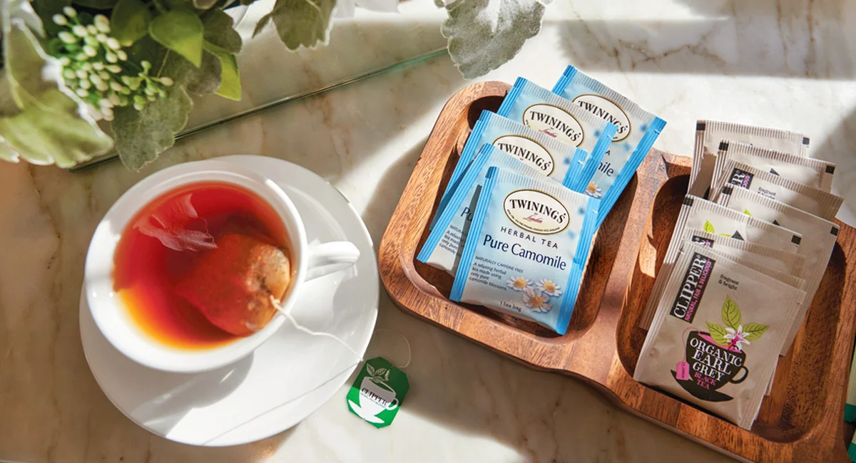A cup of tea sits next to a small tray filled with tea bags.
