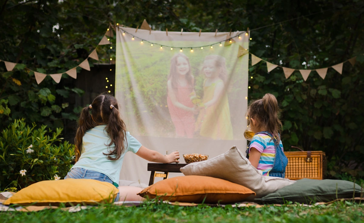 Children watching a movie on blankets and pillows outdoors on a projection screen.