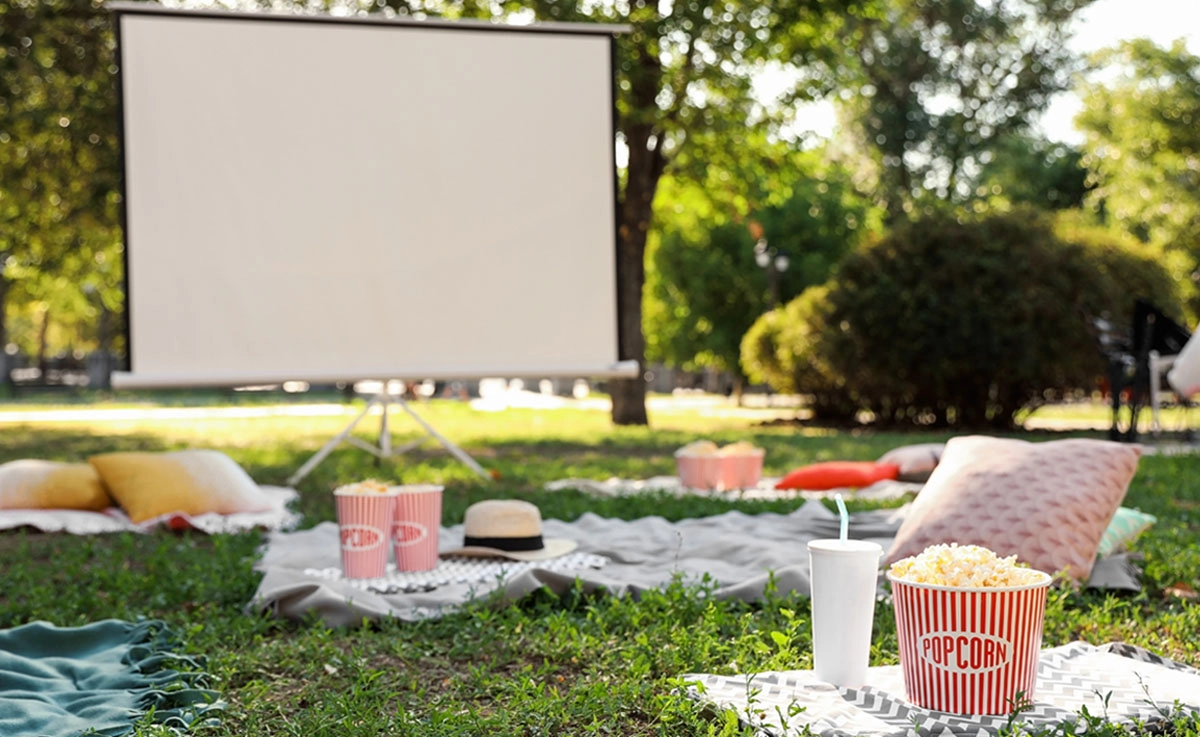 A set up for an outdoor movie night with a screen and comfortable seating on the ground.