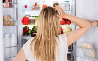 Woman staring into an open refrigerator scratching her head.