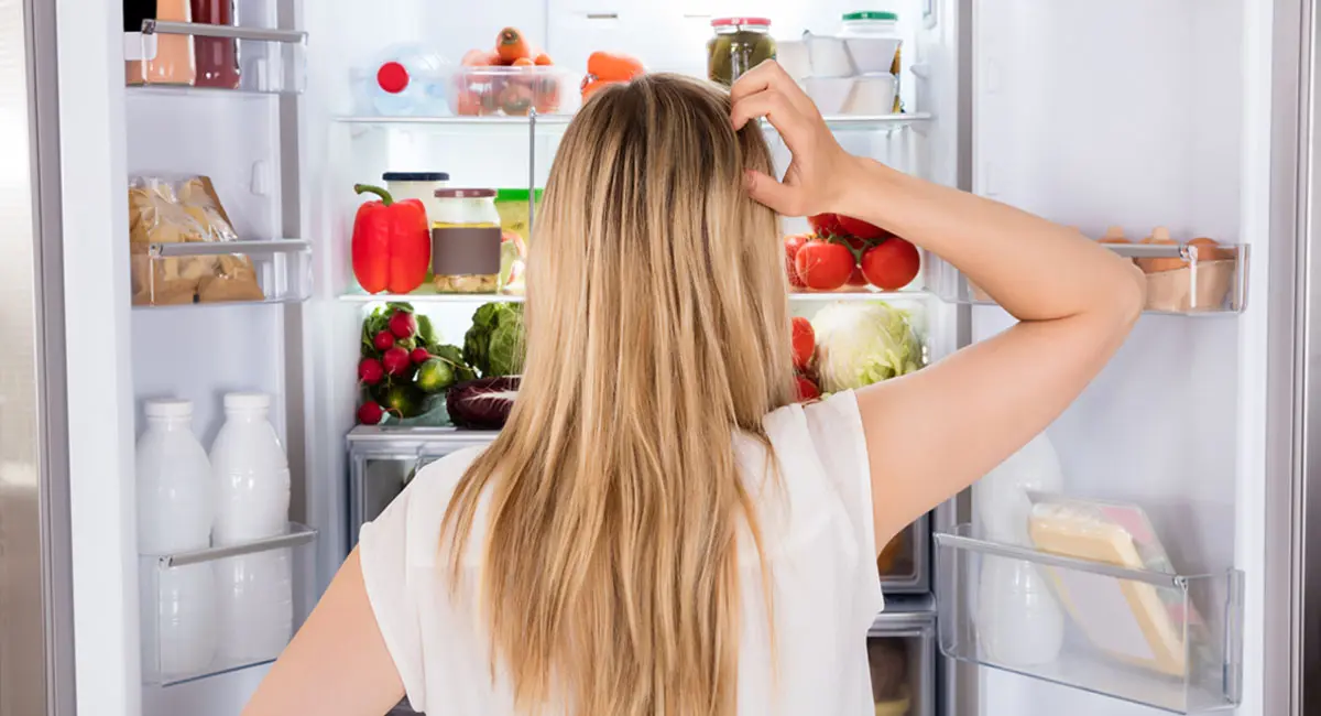 Woman staring into an open refrigerator scratching her head.