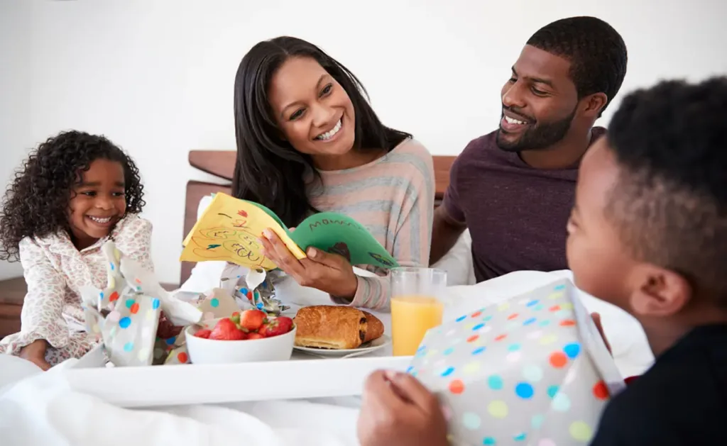 Two children and their father celebrating Mother’s Day by bringing their Mom breakfast in bed.