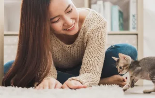 A young woman plays with a kitten on the floor.