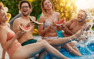 Friends hanging out by the pool eating watermelon.