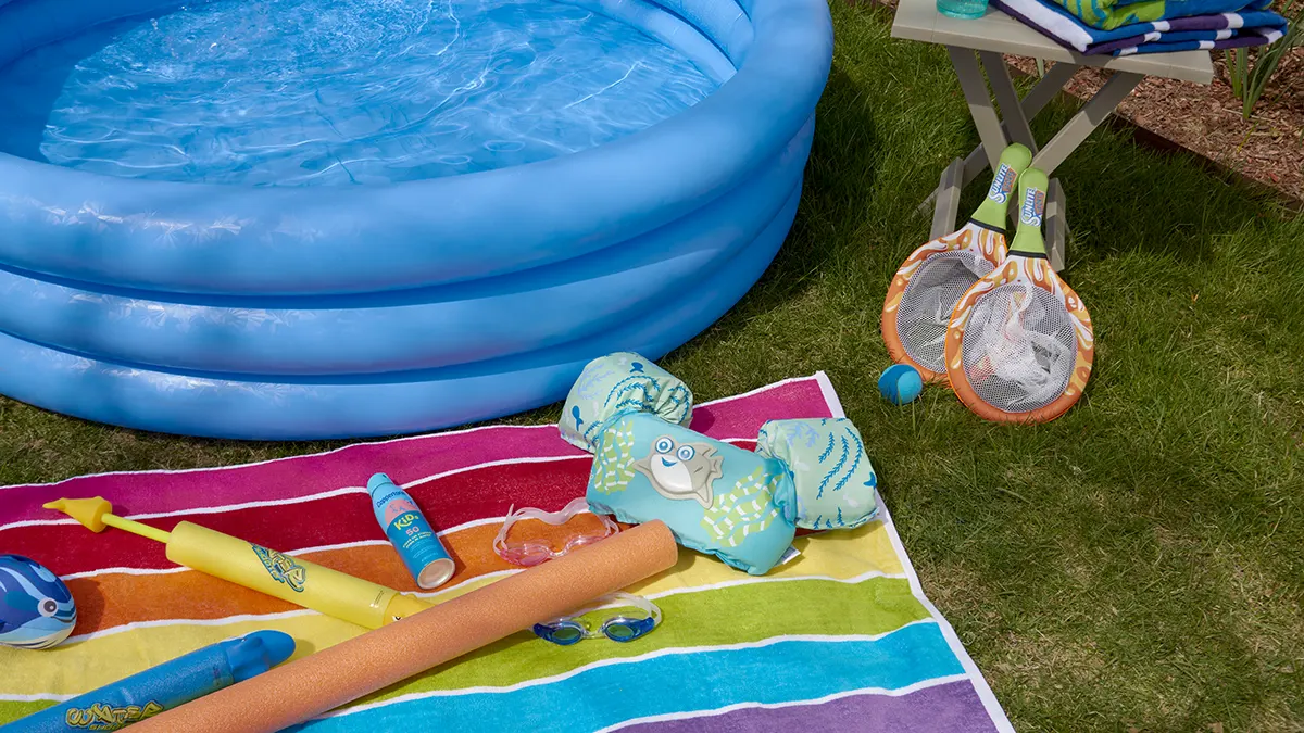 A kids portable pool surrounded by water shoes, towels, and other summer accessories.