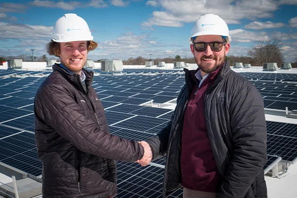 Two people shaking hands in front of a solar rooftop array.