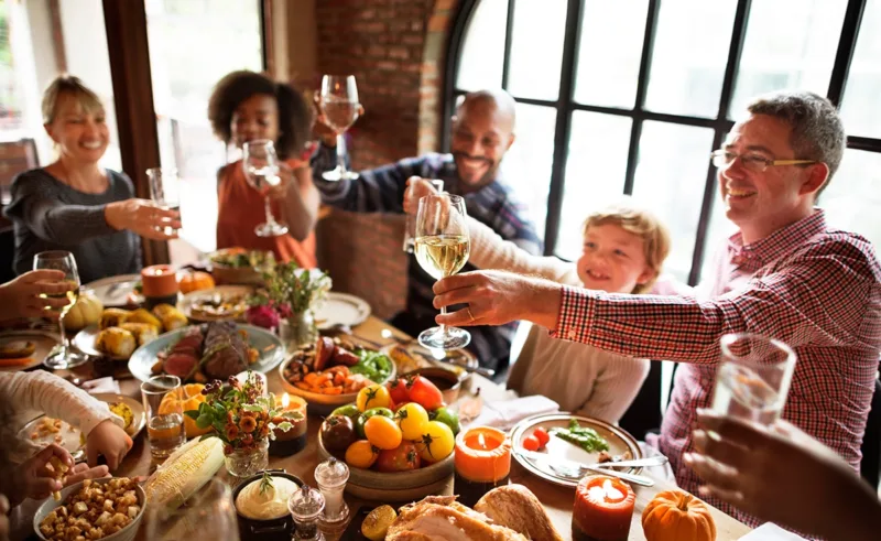 People gathered around a dining table for Thanksgiving, raising glasses to cheers.