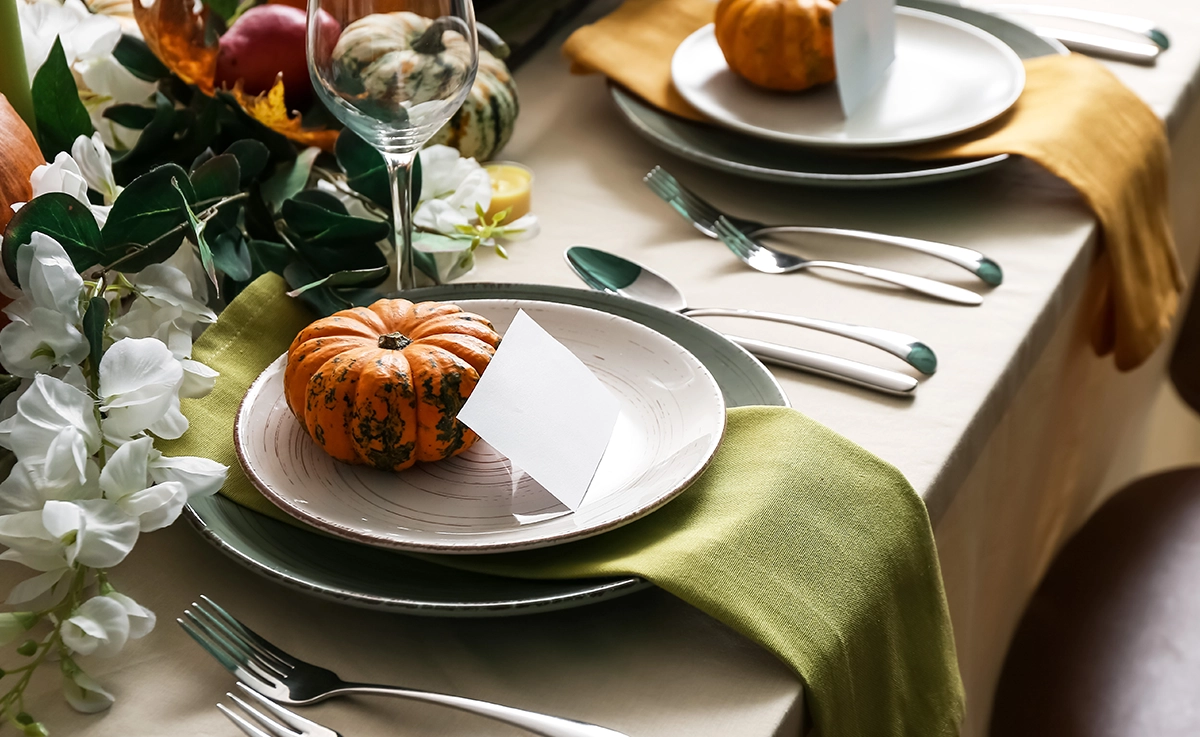 A close-up of a thanksgiving table setting with floral decor, mini pumpkins, and a place card.