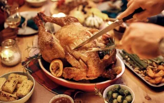 A person carving a turkey at a dinner table on Thanksgiving.