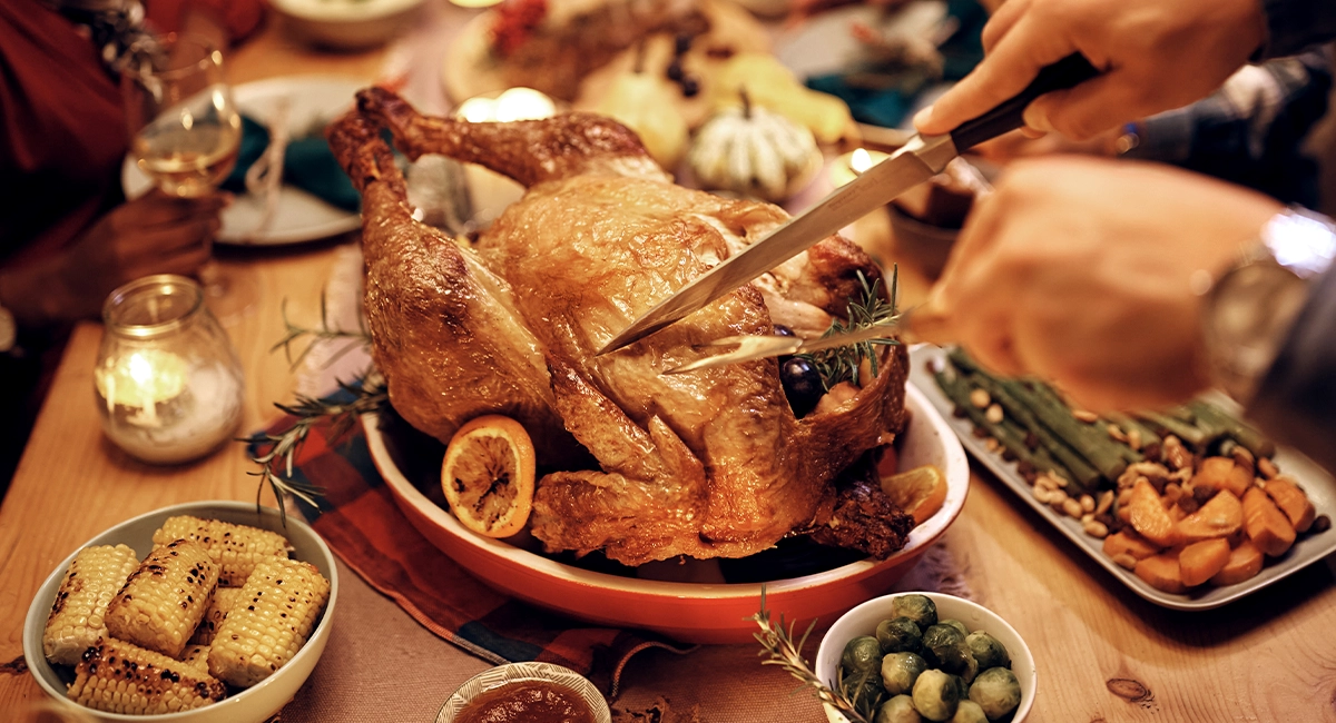 A person carving a turkey at a dinner table on Thanksgiving.