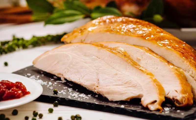 Close-up shot of carved-up roasted turkey meat on a black plate.