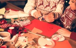 An adult and a child working on holiday crafts together at a table full of craft supplies.