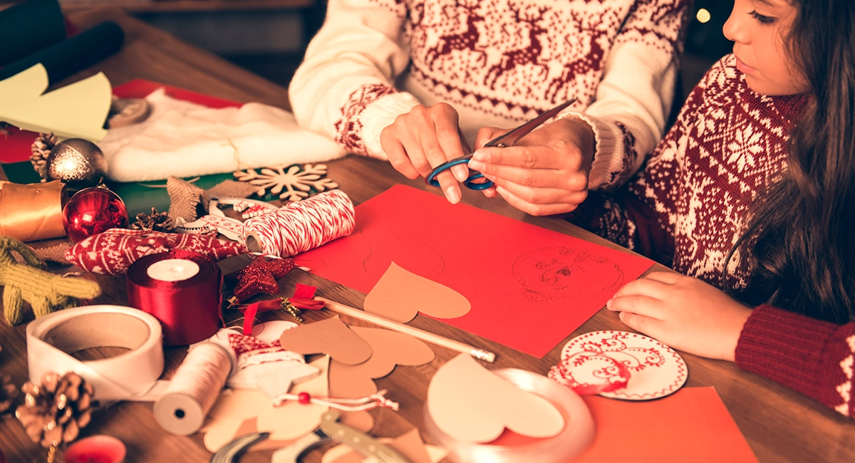 An adult and a child working on holiday crafts together at a table full of craft supplies.