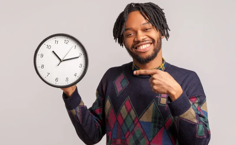 A person points to a clock that they are holding.