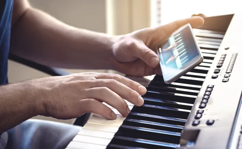 A person learning how to play the piano with a tutorial on their phone.