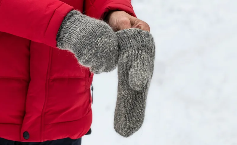 a person outside in the snow puts on a pair of mittens