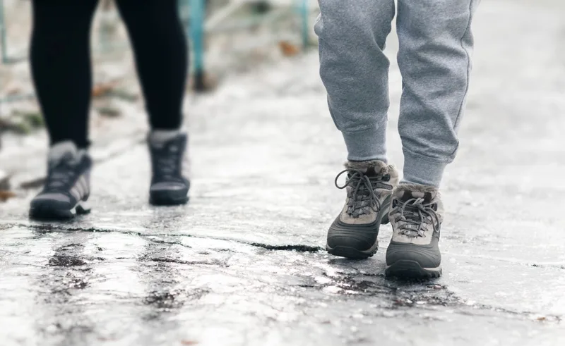 two people wearing boots, walking on a slippery sidewalk