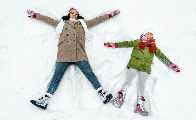 A parent and a child make snow angels together.