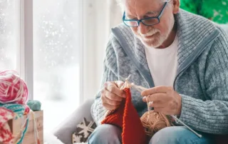 A person sits in a livingroom learning how to knit while it snows outside.