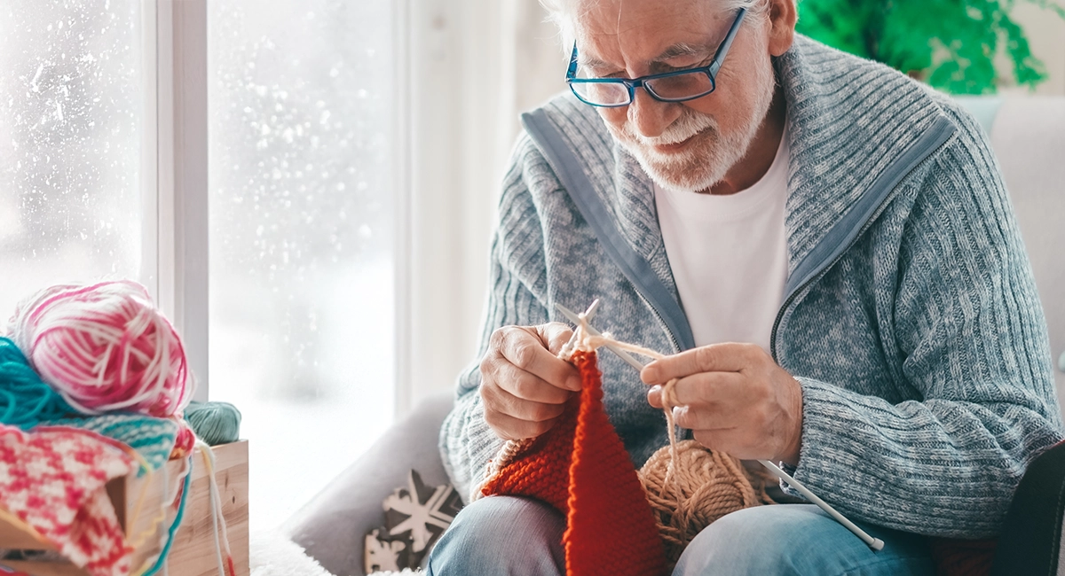 A person sits in a livingroom learning how to knit while it snows outside.