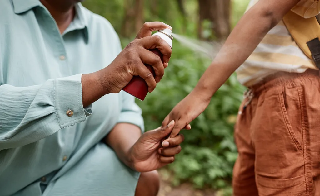 A parent sprays their child with insect repellent.