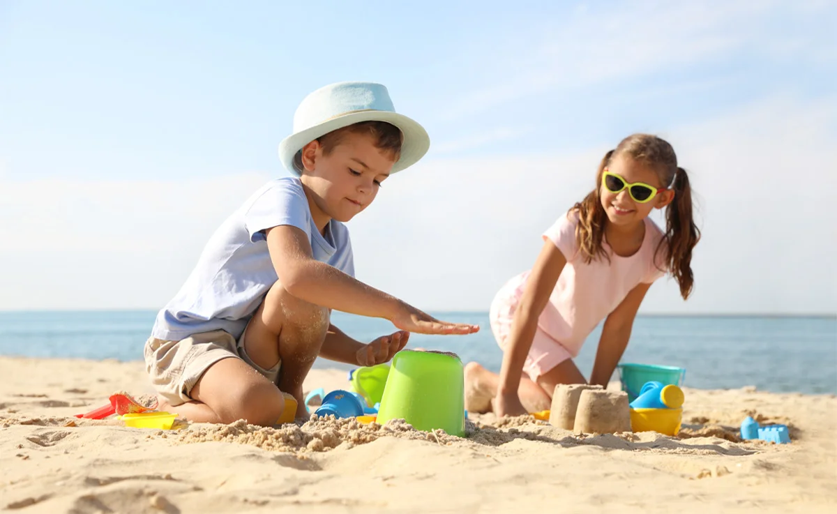 Children making sandcastles with plastic pail and toys on sandy beach