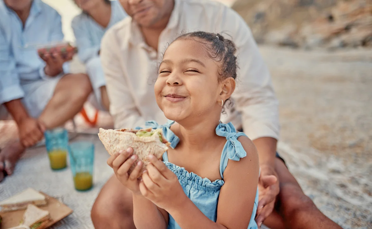 Child smiling with sandwich at beach picnic