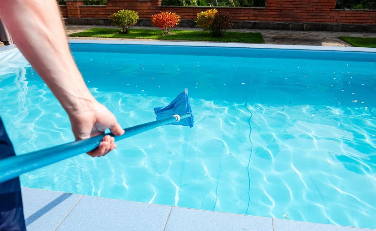Person skimming debris out of pool before closing for the season.