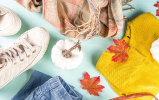 Assorted fall clothing items with tiny pumpkins and fallen maple leaves.
