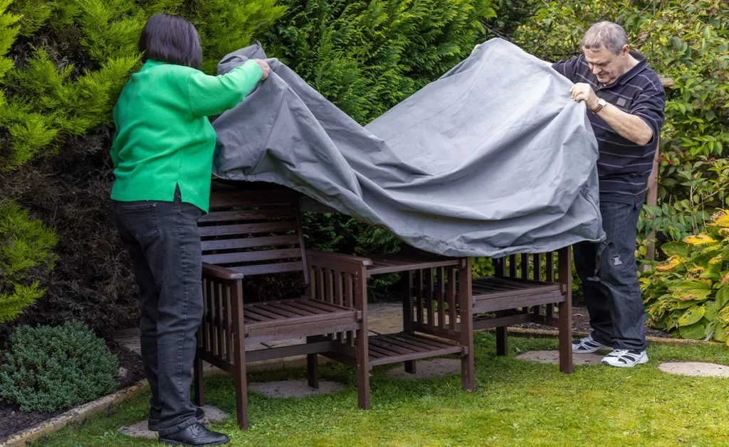 Two people cover their outdoor furniture to prepare for the coming season.