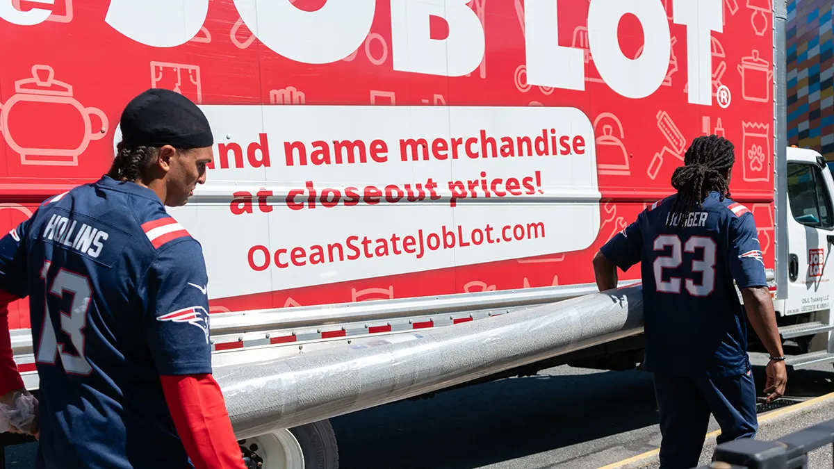 New England Patriots players carrying a rug donation off of an Ocean State Job Lot truck.