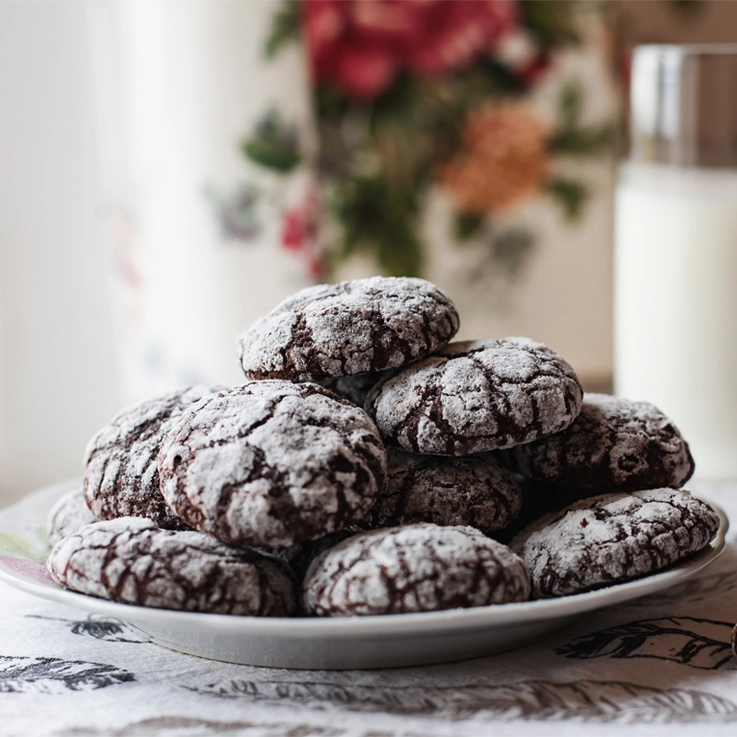 Homemade chocolate crinkle cookies with powdered sugar and glass of milk at the kitchen.