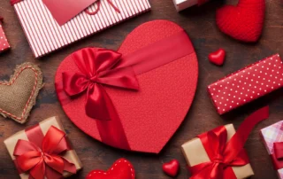 A heart shaped box of chocolates surrounded by other wrapped gifts for Valentine's Day.