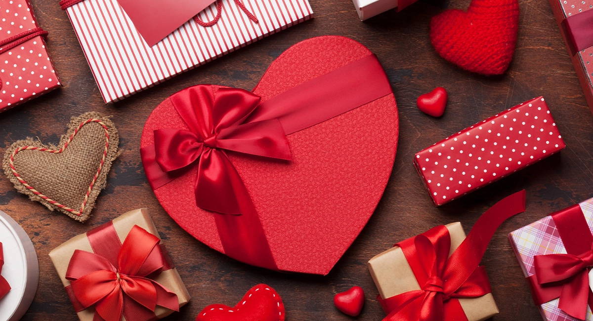 A heart shaped box of chocolates surrounded by other wrapped gifts for Valentine's Day.