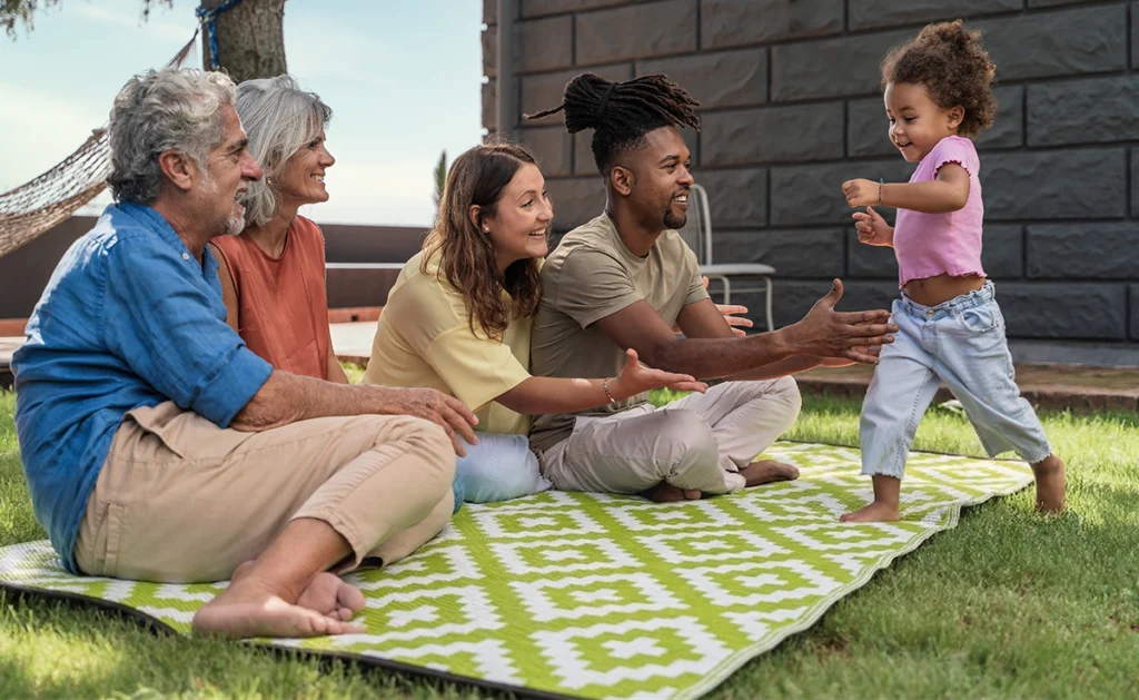 A family hanging out outside on an outdoor rug.