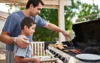 A father teaching his son how to grill hot dogs and bonding over cooking on the grill.