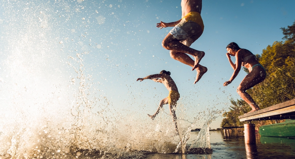 Friends jumping off of a dock into a lake. Friends jumping off of a dock into a lake.