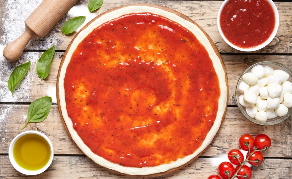 A pizza dough stretched out with sauce on top.