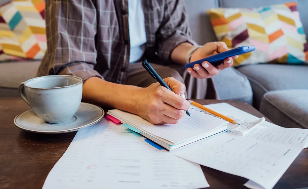 A person sits in front of a table and works on personal budgeting with papers and a calculator.